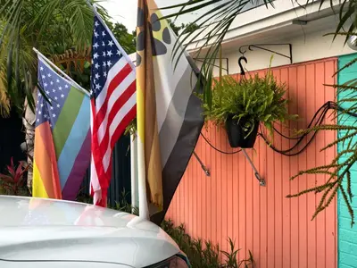 a car parked next to flags on a fence at Calypso Inn Wilton Gay Male Resort in Fort Lauderdale