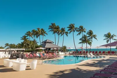 a resort pool with chairs and palm trees and the ocean at 3 Bedroom Apt Ocean-Front Resort The Alexander in Miami Beach