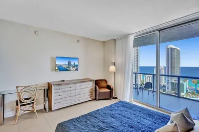 a bedroom with a bed and a desk and a large window at Sky-High Spacious Ocean View Condo 4 BDRS 3 BATH in Hallandale Beach