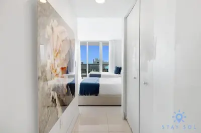 a white room with a bed and a mirror at Infinite View - Balcony - Gym - Pool in Hallandale Beach
