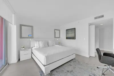 a white bedroom with a bed and a desk and a chair at Lovely 3 bedroom 3 bathroom ocean front in Hallandale Beach