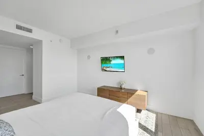 a white bedroom with a bed and a wooden dresser at Modern Ocean View 3 Bedroom Condo Resort Amenities in Hallandale Beach