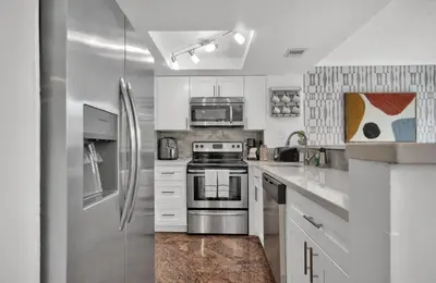 a kitchen with white cabinets and a stainless steel refrigerator at Treetop Retreat! Cozy 2 Bedroom In Heart Of Grove in Miami