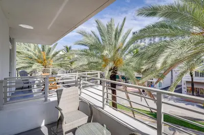 a balcony with two chairs and palm trees at Miami Beach Vacation Rental with Rooftop Pool Access in Miami Beach