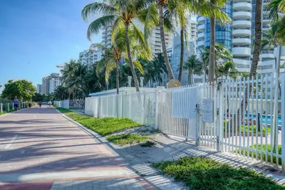 a white fence next to a sidewalk with palm trees at Deluxe Studios and Apartments at the Casablanca in Miami Beach