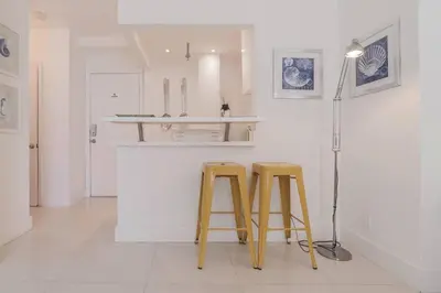 two yellow stools in a white kitchen with a counter at OCEAN & SAND ONLY 1 MINUTE WALK! in Miami Beach