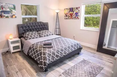 a bedroom with a bed with a gray comforter and two windows at HOUSE WITH POOL, 10 MINS DRIVE TO THE BEACH! in Miami Shores