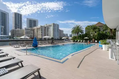 a large swimming pool with chairs and a city at Refined Oceanview Apartment, Kitchen, Comfort & Location -A in Hallandale Beach