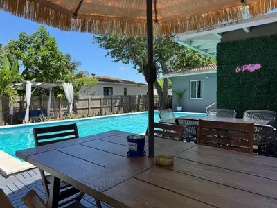 a wooden table with an umbrella next to a swimming pool at La Playita 4-BR Heated Pool Miami 16 Guests in Miami