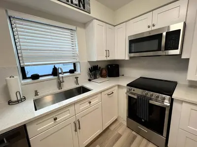 a kitchen with white cabinets and a sink and a microwave at Modern Tropical Oasis with Arcade, HotTub & MiniGolf in Hollywood