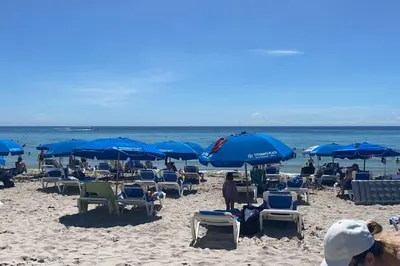 a group of people sitting on a beach with blue umbrellas at Oceanview Luxury 2BR with Pool & Beach in Hallandale Beach