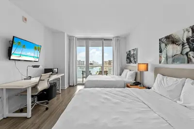 a hotel room with two beds and a desk with a computer at Water View Building With Pool - 5-Min Walk To The Beach - Cozy Studios in Hallandale Beach