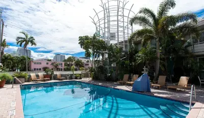 a large swimming pool with palm trees and buildings at Manhattan Tower Apartment Hotel in Fort Lauderdale
