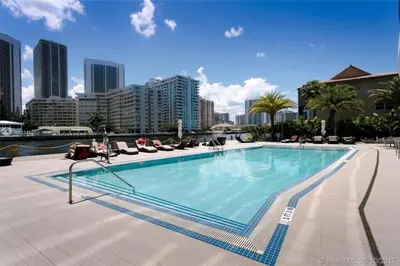 a large swimming pool with chairs and a city at Cozy Beach Apartment with Full Kitchen -A in Hallandale Beach