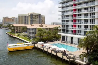a yellow boat on a river next to a building at Cozy BeachWalk Nest, 2 Full Beds, Steps to Ocean in Hallandale Beach
