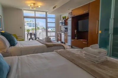 a bedroom with two beds and a television and a balcony at Rooftop-Pool Suite on Ocean Dr C505 in Miami Beach