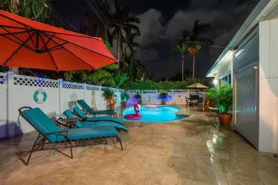 a patio with a pool with chairs and a red umbrella at ~Villa Victoria Luxury! (Pool)~1 mile from beach in Fort Lauderdale
