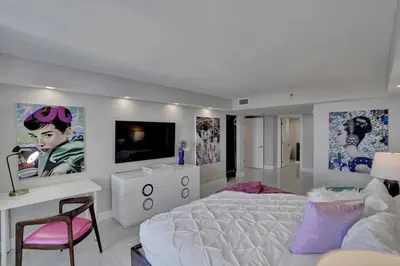 a white bedroom with a white bed and a tv at A Wave From It All! Direct water views! in Miami