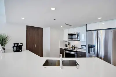 a white kitchen with a sink and a refrigerator at Feels Like Summer ~ Panoramic Water Views! in Miami