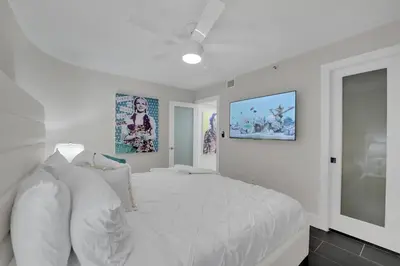 a white bedroom with a large white bed and paintings at Iconic! Miami Skyline & Water Views in Miami