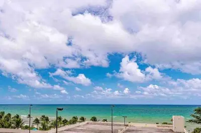 a beach with palm trees and a blue sky and clouds at Paradise Retreat, Near Beach, Casino, and More in Hollywood
