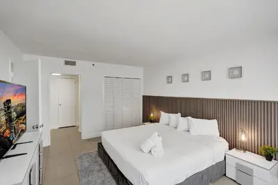 a bedroom with a large white bed and a flat screen tv at Ocean View condo w beach service 411 in Miami Beach