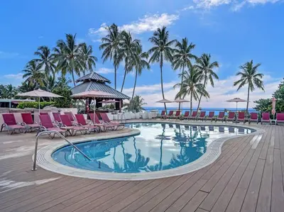 a swimming pool with chairs and palm trees and the ocean at Ocean View Condo Beach Service 1504 in Miami Beach