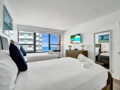a white bedroom with two beds and a window at Ocean View Condo Beach Service 1504 in Miami Beach