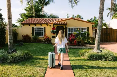 a woman walking with a suitcase in front of a house at Fun Getaway: Hot Tub, Tiki Bar, Arcade Room in Hollywood