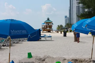 a beach with some blue umbrellas and a lighthouse at Marenas LATERAL ocean view daily refresh not included Fees collected at arrival in Sunny Isles Beach