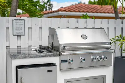 a barbecue grill with a fence in front of a house at Coconut Walk To The BeachComfy Beds Firepit Pool in Fort Lauderdale