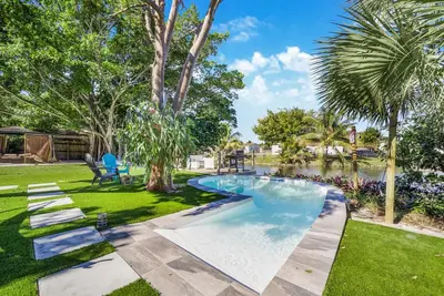 a swimming pool in a yard with a pond at Dior Lake Front Villa With Infinity Pool in Miami Gardens