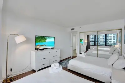 a white bedroom with two beds and a flat screen tv at Resort beach condo w beach service 601 in Miami Beach