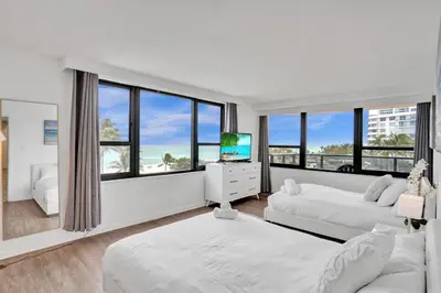 a white bedroom with two beds and a television at Resort beach condo w beach service 601 in Miami Beach