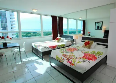 a hotel room with two beds and a desk and windows at Castle 1118 Studio BayView Direct Beach Access, Tennis, Pool, Restaurants, Free Parking in Miami Beach