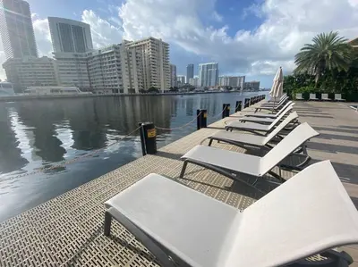 a row of white lounge chairs next to a body of water at Modern Miami Studio with 2 full beds, Cozy & Convenient in Hallandale Beach