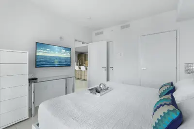 a white bedroom with a bed and a tv on the wall at Tiffany Ebony - Ocean & Canal views, Walk to Beach in Fort Lauderdale