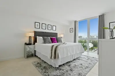 a white bedroom with a bed and a large window at Tiffany Sage - Rooftop Pool, Gym, & Walk to Beach in Fort Lauderdale
