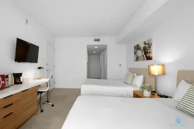 a hotel room with two beds and a desk and a tv at Upper studio with Balcony - Pool - Gym in Hallandale Beach