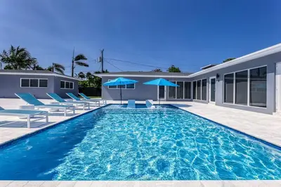 a swimming pool with blue chairs and a house at Sunshine Manor 2017-1 in Fort Lauderdale