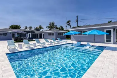 a swimming pool with chairs and blue umbrellas at Sunshine Manors 2017-3 in Fort Lauderdale