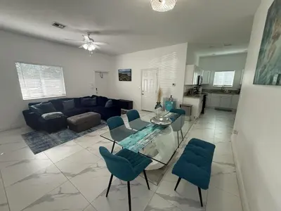 a living room with a glass table and blue chairs at Mango Haus Near Beach, Cruise Port & Stadium in Fort Lauderdale