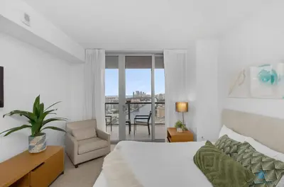 a bedroom with a bed and a chair and a window at Amazing view - Balcony - Gym - Pool in Hallandale Beach