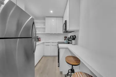 a white kitchen with a refrigerator and a wooden stool at Mykonos Home - 2 2 Cozy and Charming Duplex in Miami