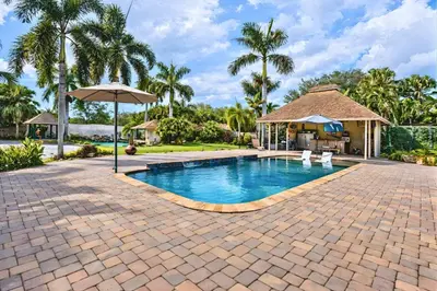 a swimming pool with an umbrella and palm trees at Villa Fiesta - Celebrate Dreams Create Memories in Southwest Ranches