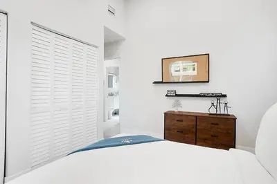 a white bedroom with a bed and a wooden dresser at Breathtaking Pool Home and Backyard by Wilton Mnrs in Fort Lauderdale