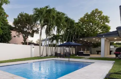 a swimming pool with an umbrella and palm trees at Miami Getaway Heated Pool Villa with Mini Golf & BBQ in Miami