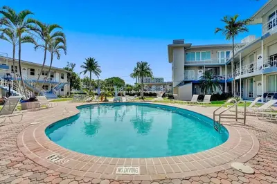 a swimming pool with palm trees and buildings at Vistamar Waterfront Beach Abode -Walk to the Beach in Fort Lauderdale