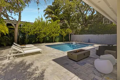 a backyard with a swimming pool with chairs and a table at Designer Home w Pool & Firepit - 7 min to Brickell in Miami