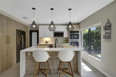 a kitchen with two white bar stools and a kitchen island at Designer Home w Pool & Firepit - 7 min to Brickell in Miami